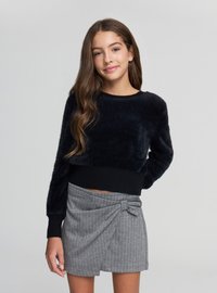 Czarny, puszysty krótki sweter z długimi rękawami i prążkowanym dołem; zestawiony z szarą spódnicą z zakładkami w drobne prążki, ozdobioną węzłem.