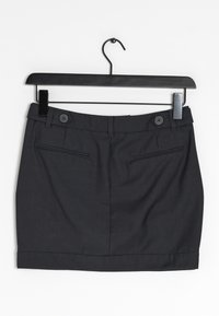 Musta hame, jossa on istuva malli, vyötärönauha, kaksi etutaskua ja hieman käännetty helma. Valmistettu sileästä kankaasta, jossa on hieno rakenne.