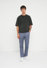 Čierna nadrozmerná košeľa s krátkym rukávom v kombinácii s svetlomodrými slim-fit nohavicami a bielymi teniskami, umiestnená na jednoduchom bielom pozadí.