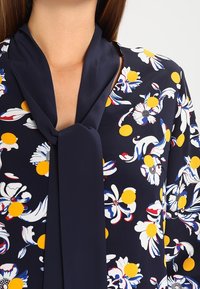 Mekko merenkulkijoille, jossa on kukkakuosi, joka esittelee keltaisia ympyröitä ja valkoisia kukkia. Sidottu kaulaosa ja sileä kangas.