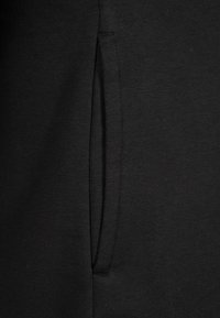 Tissu en sweatshirt noir avec une surface texturée, présentant une poche latérale et sans logos ni motifs visibles. Design simple et fonctionnel.