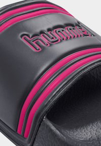 Svart slide-sandal av slätt syntetiskt material, med en upphöjd logotyp och två rosa ränder tvärs över ovandelen för kontrast.