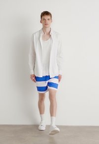 White long-sleeve shirt over a plain white tank top, paired with blue and white striped shorts. White sneakers and visible ankle socks.