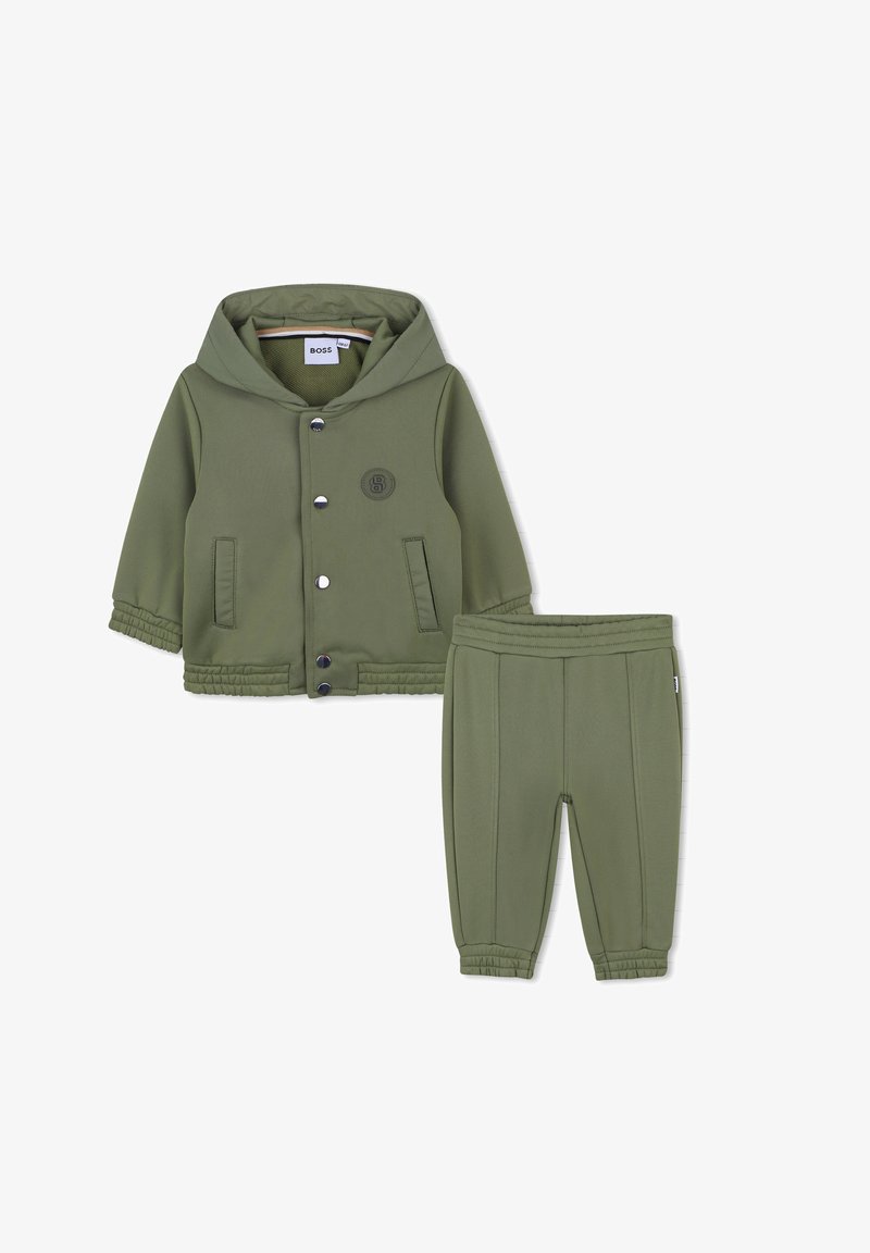 Oliwkowy dwuczęściowy strój z kapturem, obejmujący kurtkę zapinaną na zatrzaski oraz dopasowane spodnie o tapered cut z elastycznym pasem.