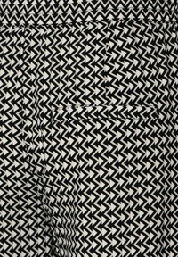 Svart och vit zigzag-mönstrad tyg med en liten fickdetalj, som visar en geometrisk design och en mjuk textur.