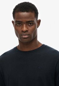 Marineblauwe katoenen crewneck t-shirt met korte mouwen en een klein, geborduurd logo op de borst. Glad materiaal en eenvoudig ontwerp.