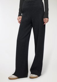 Pantaloni ampi grigio scuro realizzati in materiale morbido, con vita alta e vestibilità comoda, abbinati a sneakers chiare.