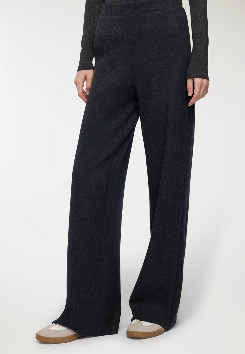 Pantaloni ampi grigio scuro realizzati in materiale morbido, con vita alta e vestibilità comoda, abbinati a sneakers chiare.