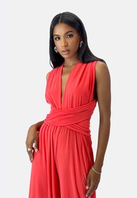 Jumpsuit rosso senza maniche con scollo a V profondo e vita arricciata. Realizzato in tessuto morbido, presenta gambe ampie e fluide con una superficie liscia.