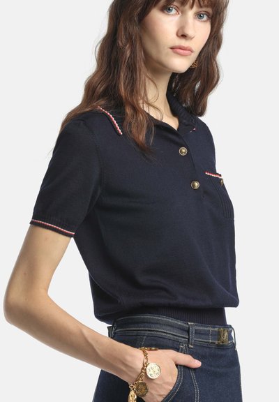 Tricou polo bleumarin tricotat, cu guler și nasturi aurii. Are borduri roșii și albe pe guler și mâneci. Buzunar pe partea stângă.