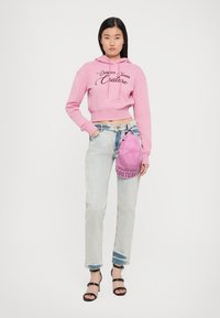 Felpa corta rosa con lettering testurizzato, jeans blu chiaro a vita alta e borsa rosa, abbinati a tacchi neri con cinturini.
