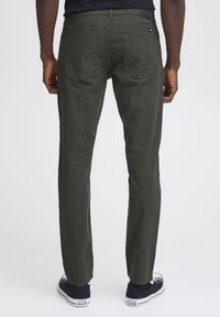 Pantalones rectos grises de textura suave, con dos bolsillos traseros y sutiles detalles de costura, combinados con zapatillas de deporte azules.