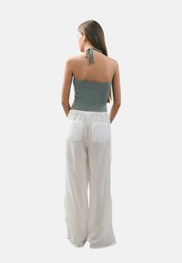 Top corto acanalado gris claro con cuello halter atado, combinado con pantalones de pierna ancha blancos que tienen dos bolsillos traseros y una tela suave y texturada.