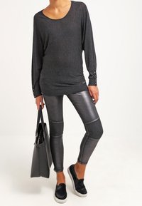 Top ligero negro de manga larga con un escote amplio. Leggings gris metálico con variaciones de textura. Zapatos negros sin cordones y bolsa tote.