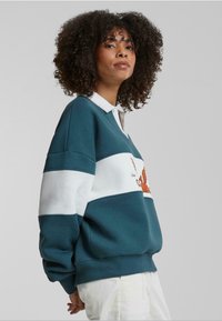 Sweatshirt teal și alb cu guler, având un design grafic în nuanțe de portocaliu și maro. Croială lejeră și material texturat.