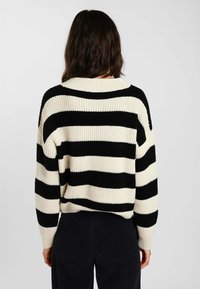 Maglione a maglia con righe nere e crema, caratterizzato da un ampio scollo rotondo e da polsini a coste. Vestibilità rilassata con un materiale testurizzato e spesso.
