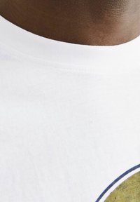 Tricou alb din bumbac, cu decolteu rotund, având un design grafic circular în accente de verde și albastru stins. Textura moale este vizibilă.