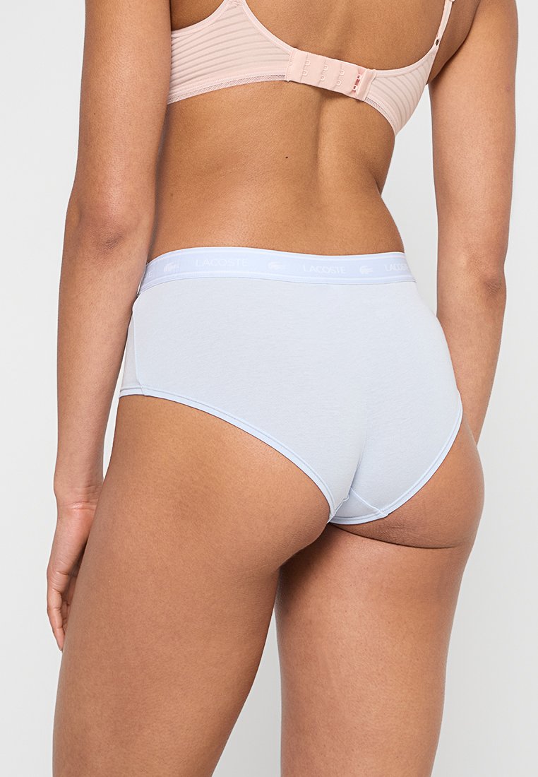 Helle blauen Baumwollslips mit einer sanften Textur und einem breiten, elastischen Bund, der das Lacoste-Logo trägt. Die Rückansicht zeigt ein nahtloses Design.