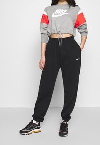 Gray cropped sweatshirt with red and white accents, black sweatpants, and multicolor sneakers, featuring a drawstring and logos.