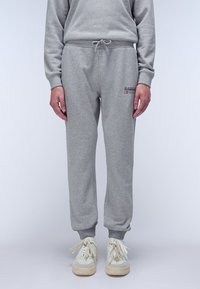 Grijze sweatpants gemaakt van zachte stof met een elastische tailleband en boorden, met een logo patch op de linkerheup. Gecombineerd met lichte sneakers.