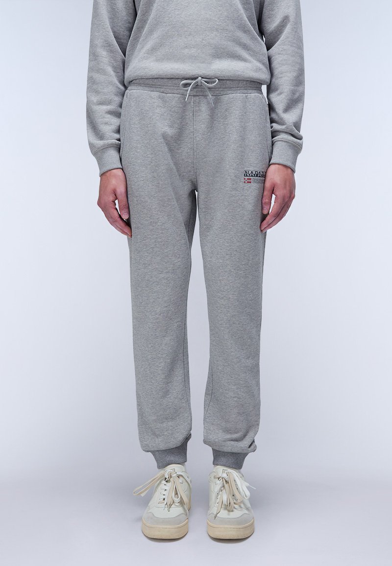 Grijze sweatpants gemaakt van zachte stof met een elastische tailleband en boorden, met een logo patch op de linkerheup. Gecombineerd met lichte sneakers.