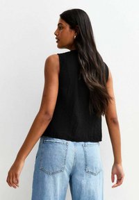 Svart ärmlös topp i texturerat tyg, tillsammans med ljusblå denimjeans med bakfickor och en avslappnad passform.