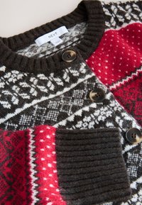 Neuletakki, jossa on monivärinen kuviointi tummanruskealla, punaisella ja valkoisella. Mukana kaksi nappia ja teksturoitu tasku.