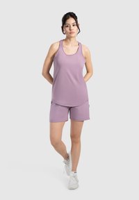 Top de entrenamiento morado y pantalones cortos de tejido transpirable, con un escote redondo y un corte holgado, combinados con zapatillas blancas.
