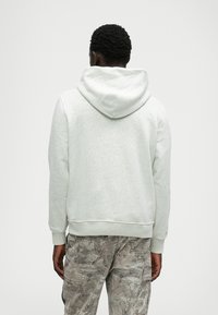 Helles graues Hoodie mit einer Kordelzugkapuze, gerippten Bündchen und Saum, kombiniert mit gemusterten Cargo-Hosen, die eine weiche Textur und ein lässiges Design zeigen.