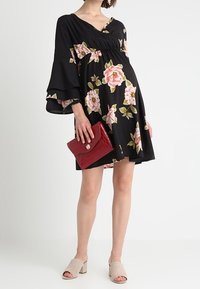 Černé květinové šaty s volánovými rukávy, zdobené růžovými růžemi. Kombinované s červenou kabelkou a světle béžovými sandály na blokovém podpatku.