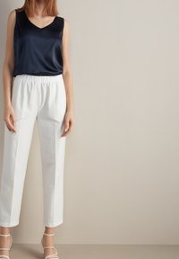 Marinblus i satin utan ärm med V-ringning, ihop med vita, högmidjade byxor med avslappnad passform och elastisk midja.