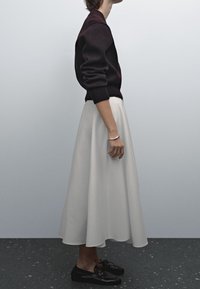 Una modella indossa un maglione nero con scollatura rotonda, abbinato a una gonna midi bianca fluida e scarpe nere con lacci.