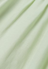 Tissu vert pâle avec une texture douce et un tissage fin visible, présenté en plis doux créant des ombres subtiles.
