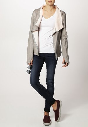 Lys grå lynlåsjakke med lyserød inderside, båret over en hvid V-hals t-shirt, parret med mørke jeans og kastanjebrune slip-on sko.