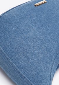Denim laptop sleeve med en buet form, blå stoftekstur og et sølvfarvet mærke. Detaljeret syning langs kanterne.