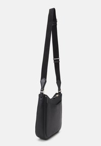 Sort læder skuldertaske med struktureret overflade, justerbar canvasrem og forlommer. Har en lynlåslukning og glatte detaljer.