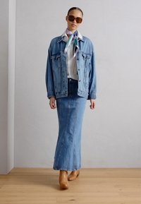 Spijkerjack, witte blouse, lange spijkerrok, bruine haklaarzen en een gebloemde sjaal. Accessoires zijn onder andere bruine zonnebril.
