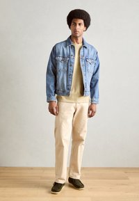 Vaaleansininen farkkutakki, vaaleanbeige paita alla, kermaväriset housut ja tummanvihreät kengät, joiden pinnassa on kuvio.