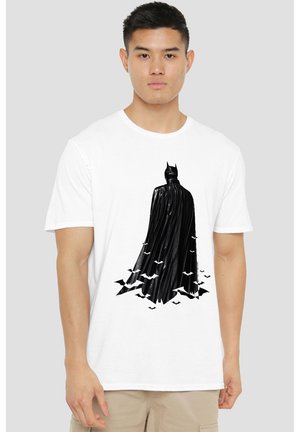 Junger Mann trägt ein weißes T-Shirt mit schwarzer Batman-Silhouette von hinten, umgeben von fliegenden Fledermäusen am unteren Rand des T-Shirts.