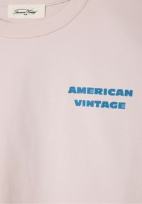 Svijetlo ružičasti dukserica s natpisom "AMERICAN VINTAGE" u podebljanim plavim slovima. Mekana tekstura, okrugli izrez i rebrasti manžeti.