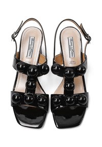 Sandali in vernice nera con tre grandi accenti rotondi nella parte anteriore, design open-toe, cinturino regolabile alla caviglia e tacchi quadrati.