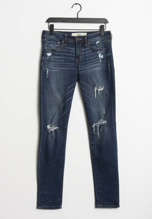 Tmavě modré denimové skinny džíny s několika roztrhnutími a třepenými okraji. Mají pět kapes a zapínání na zip, pověšené na černém ramínku.