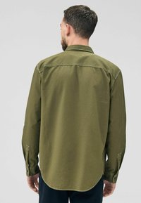 Man wearing a dark green, textured long-sleeve shirt, viewed from the back, standing against a plain light gray background.