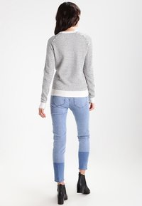 Vit och svart mönstrad tröja med rund halsringning, kombinerad med ljusblå jeans med färgblockade detaljer och svarta ankelskor.