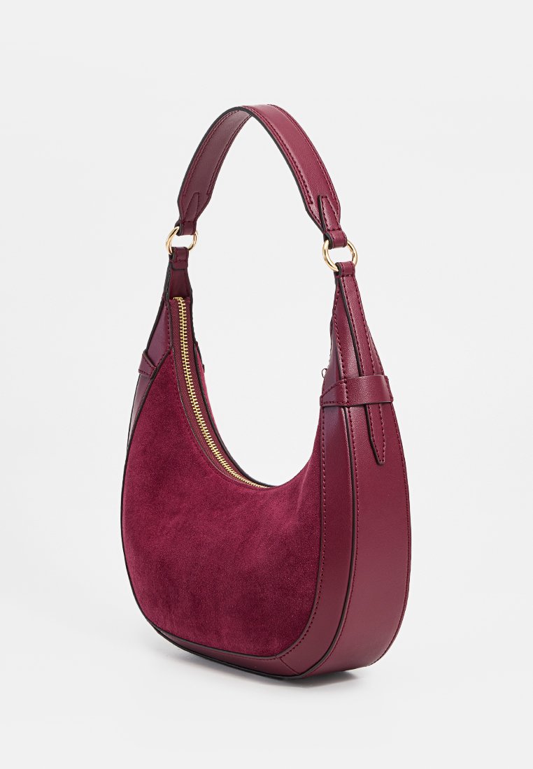Sac à main en cuir et daim bordeaux avec une forme incurvée, détail de fermeture éclair doré et une seule bandoulière. Texture lisse avec des accents cousus.