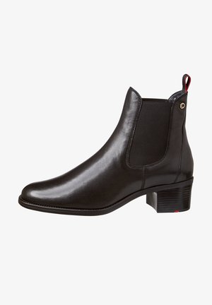 Bottine Chelsea en cuir noir avec panneaux latéraux élastiques, petit talon carré et languette rouge à l'arrière.