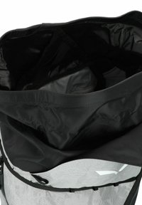 Zaino con design roll-top realizzato in tessuto nero e grigio. L'interno è rivestito in materiale grigio liscio e include tasche organizzative.