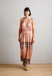 Robe maxi en tissu rose clair avec ourlet à motif, design col halter, taille cintrée et accents imprimés contrastants. Accompagnée d'un sac orange.