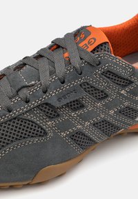 Gray suede athletic shoe with mesh panels, orange accents, and thick gray laces. The sole is brown with rubber grip studs.