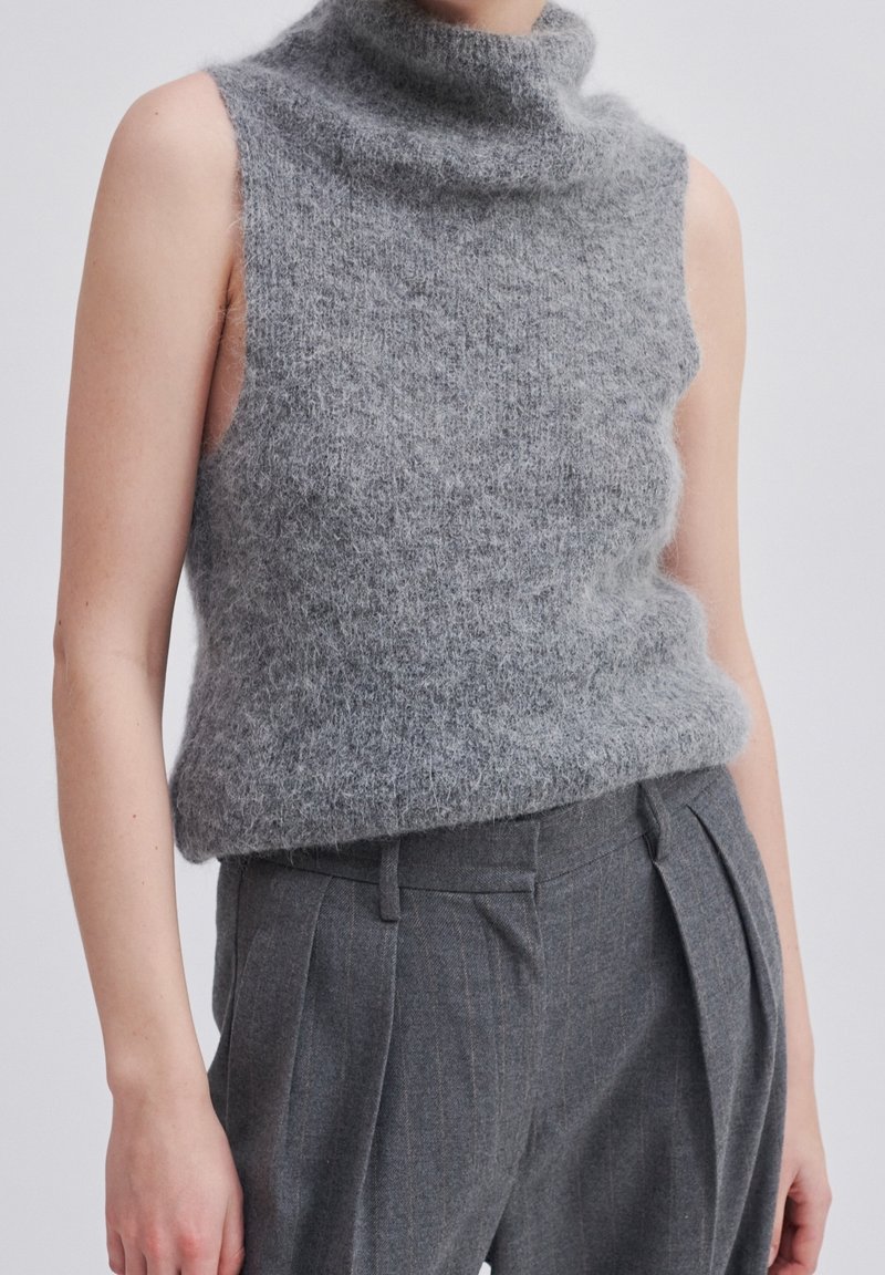 Grå ärmlös polokrage-tröja gjord av luddig, texturerad fleece, kombinerad med grå veckade byxor.